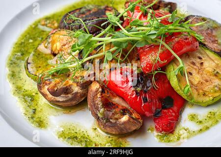 Grilled baked vegetables, eggplant, zucchini, bell pepper, champignon mushrooms, on a white plate against a dark background, with microgreen Stock Photo