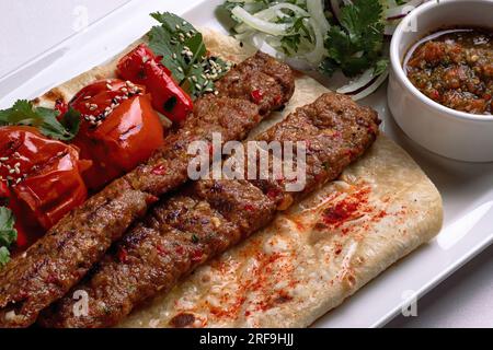 Lamb lula kebab, with baked tomatoes, onions and sauce, on a white plate, on a white background Stock Photo