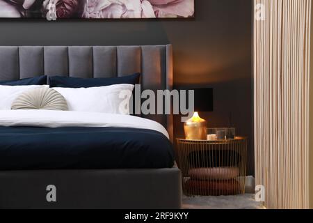 Comfortable bed with cushions, lamp and different decor on bedside table in room. Stylish interior Stock Photo