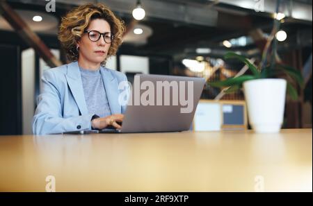 business woman working on a laptop in a coworking office. Mature business woman working on a project online. Female professional working remotely. Stock Photo