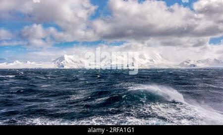 Gale force winds creating rough seas on a cold day in the southern Atlantic ocean, with a view of the South Shetland Islands coastline in Antarctica. Stock Photo