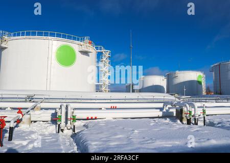 Large white iron metal industrial tanks for storage of fuel, gasoline and diesel and pipeline with valves and flanges at the refinery in the winter. Stock Photo
