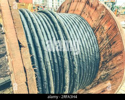 reel made of wood at a construction site. a black, long cable is wound on the coil to create communications. wires for laying in a new microdistrict. Stock Photo