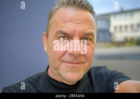 Attractive man looking critically at the camera while taking a selfie in front of a city Stock Photo