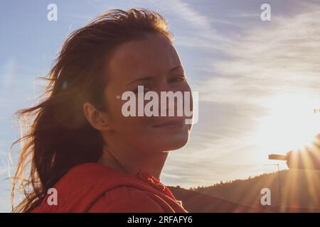 Smiling girl in sunlight. Portrait of beautiful woman on sunset. Happy tourist in evening dusk. Happy pilgrim looking at camera. Active lifestyles. Stock Photo