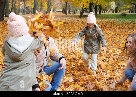 Parents with daughters play in the autumn park. Children and parents throw autumn leaves at each other. Horizontal photo Stock Photo