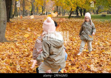 Father and daughters play in the autumn park. Children toss and throw leaves up. Horizontal photo Stock Photo