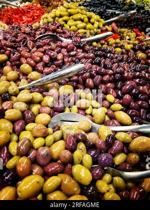 A salad bar serving pickles, peppers, and olives with scoops Stock Photo