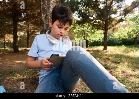 Focused serious teenager boy engaged on doing homework, studying online on a digital tablet. The concept of back to school. Online communication and d Stock Photo