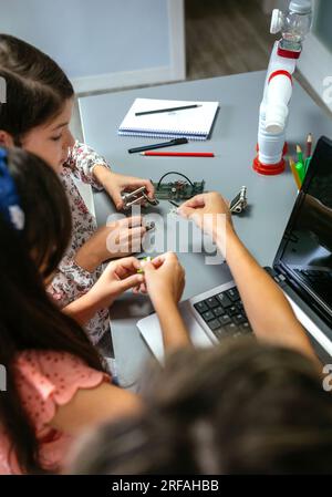 Unrecognizable female teacher helping girl students to assemble pieces of machine in a robotics class. Elementary technological education concept. Stock Photo