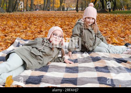 Two twin sisters lie on a blanket in the autumn park. Horizontal photo Stock Photo