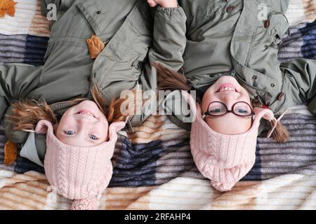 Two happy twin sisters lie on a blanket in an autumn park. The girls smile and look at the camera. View from above Stock Photo