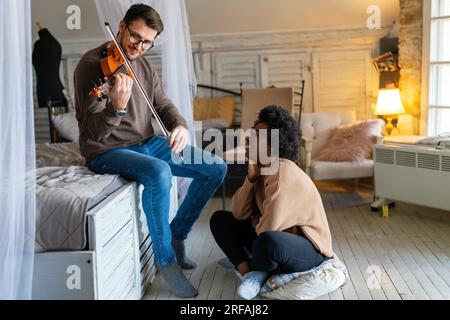 Private male music teacher giving violin lessons to a woman at home. Couple love romance concept. Stock Photo
