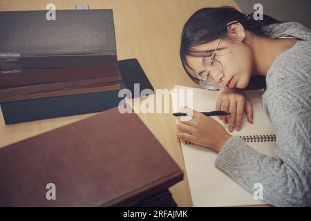 Tired student girl with glasses lying on books in library. Stock Photo