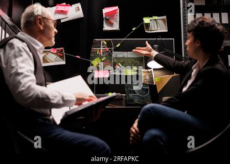 Senior private detective analyzing missing person case, discussing crime scene evidence with woman investigator. Criminology department employees working late at night in arhive room Stock Photo