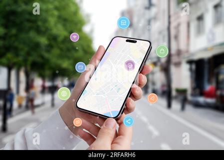 Find a location via a phone concept. Map of city on phone display with icons and network nodes flying arround Stock Photo