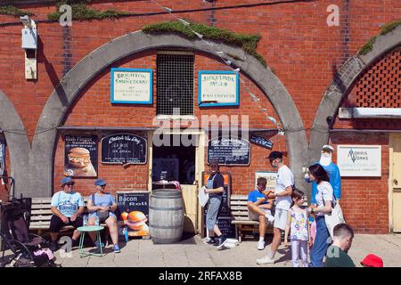 England, East Sussex, Brighton, Smokehouse fish sandwich vendor in arches by seafront promenade busy with summer tourists. Stock Photo