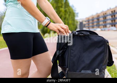 Athlete woman opening a sport bag in a park bench for workout outdoors. Wellness and fitness music for sports training exercise. Stock Photo