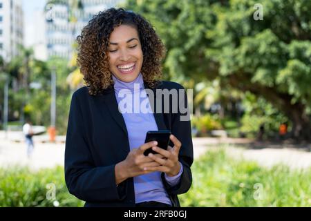 Laughing mexican businesswoman sending message at phone outdoor in city Stock Photo