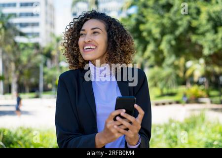 Happy mexican businesswoman sending message at phone outdoor in city Stock Photo