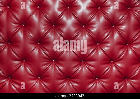 Close up background texture of red genuine leather, classic retro Chesterfield style, furniture upholstery with deep diamond pattern and buttons Stock Photo