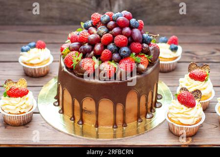 Chocolate cake with berries dipped into melted chocolate surrounded by vanilla cupcakes with cream cheese frosting Stock Photo