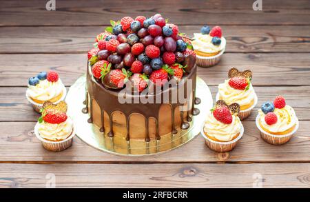 Chocolate cake with berries dipped into melted chocolate surrounded by vanilla cupcakes with cream cheese frosting Stock Photo