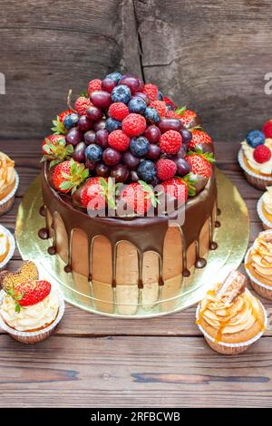 Chocolate cake with berries dipped into melted chocolate surrounded by vanilla cupcakes with cream cheese frosting Stock Photo