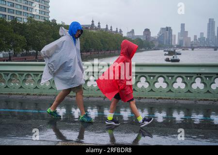 London UK. 2 August 2023   Pedestrians on Westminster bridge brave the lashing  rain and blustery conditions as the Met office issues yellow warnings  for strong winds in the UK. Credit amer ghazzal/Alamy Live News Stock Photo