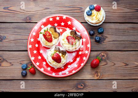 Set of vanilla cupcakes decorated with fresh strawberries, blueberries, chocolate hearts and golden sprinkles on red star plate Stock Photo