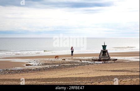 An onlooker by The Spirit of Happisburgh time and tide installation on the beach between low and high water mark at Happisburgh, Norfolk, England, UK. Stock Photo