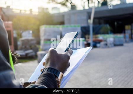 rear view of unrecognizable african ethnicity man standing using phone with construction site in background, industry concept, copy space Stock Photo