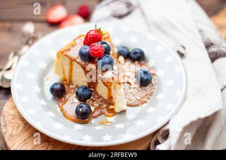 Slice of vanilla cheesecake with salted caramel sauce, fresh raspberry, blueberry and nuts on grey star plate, close up view Stock Photo