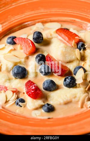 Oatmeal with blueberries, almonds and strawberries in an orange plate. Close-up. View from above. Stock Photo