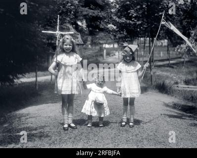 Trois petites filles, en robes de dentelle, portant croix, panier et fanion pour une procession. Bretagne (France), photographie 1921-1922. Stock Photo