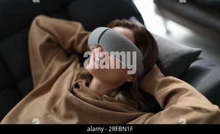 Tired woman uses massager while lying on sofa Stock Photo