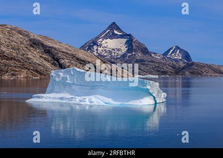 beautiful arctic landscape image of  iceberg floating past rocky mountains with snow reflected in the still water of prince christian sound greenland Stock Photo