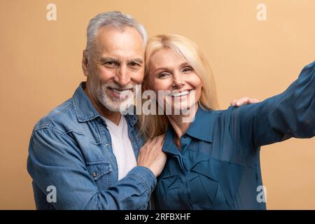 Happy attractive senior couple taking selfie, cuddling on colorful background Stock Photo