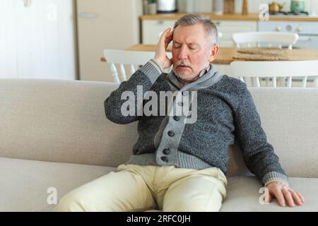 Headache pain. Unhappy middle aged senior man suffering from headache sick rubbing temples at home. Mature old senior grandfather touching temples experiencing stress. Man feeling pain hurt in head Stock Photo