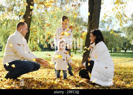 A family of four spend time in the autumn park. family throwing leaves up. Horizontal photo Stock Photo