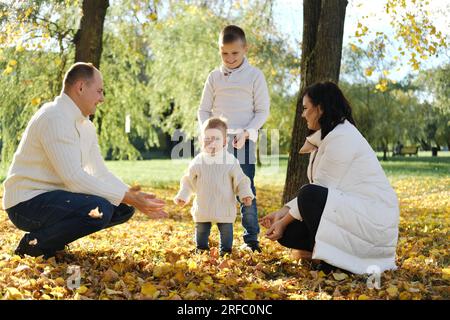 A family of four spend time in the autumn park. The family throws leaves up, entertaining the youngest son. Horizontal photo Stock Photo