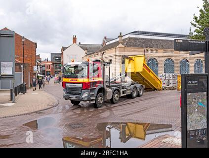 Lindum Waste lorry collecting full builders skip from building site, City Square Waterside South, Lincoln city, Lincolnshire, England, UK Stock Photo