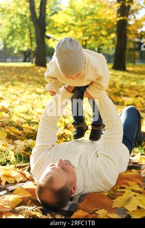 Portrait of a happy family resting in the autumn forest. Dad picks up his son in his arms while lying down on blanket. Vertical photo Stock Photo