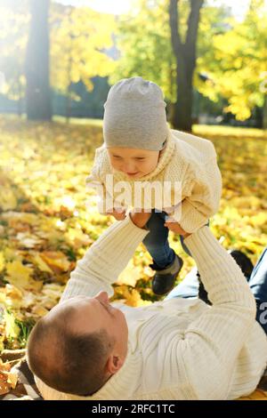 Portrait of a happy family resting in the autumn forest. Dad picks up his son in his arms while lying down on blanket. Vertical photo Stock Photo