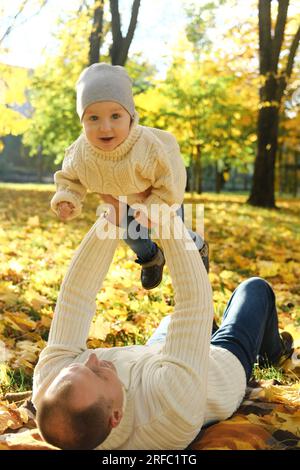 Portrait of a happy family resting in the autumn forest. Dad picks up his son in his arms while lying down on blanket. Vertical photo Stock Photo