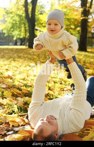 Portrait of a happy family resting in the autumn forest. Dad picks up his son in his arms while lying down on blanket. Vertical photo Stock Photo