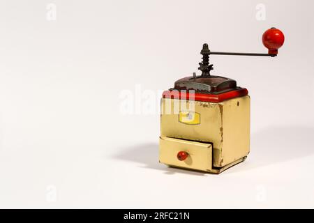 Old wooden colored manual coffee grinder with red handle, on white background, with copy space. Stock Photo