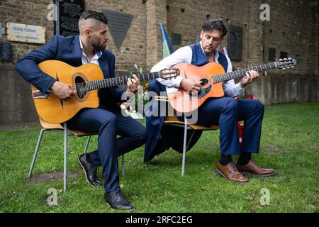 02 August 2023, Brandenburg, Fürstenberg/Havel: Marlon Reinhardt (from left) and Taylor Swing (from right) play guitar at the event for a new memorial plaque for Sinti and Roma in Ravensbrück . There is a new memorial plaque at the Ravensbrück Memorial for Sinti and Roma who were deported to the concentration camp during the Nazi era. Photo: Hannes P. Albert/dpa Stock Photo