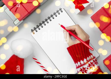Woman Writing in an Empty Notebook on White Desk. Girl's Hands with Pencil Among Red Gift Box and Winter Festive Decor. Concept of Diary, Holiday Gree Stock Photo
