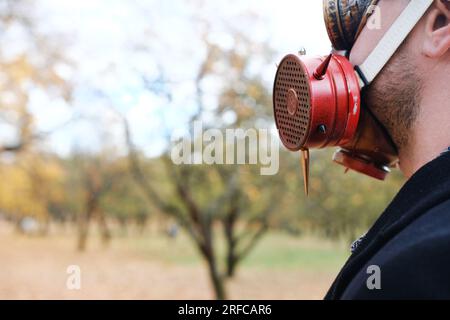 A man in a gas mask and steampunk goggles stands with his back to the camera and looks at his surroundings. Horizontal photo Stock Photo